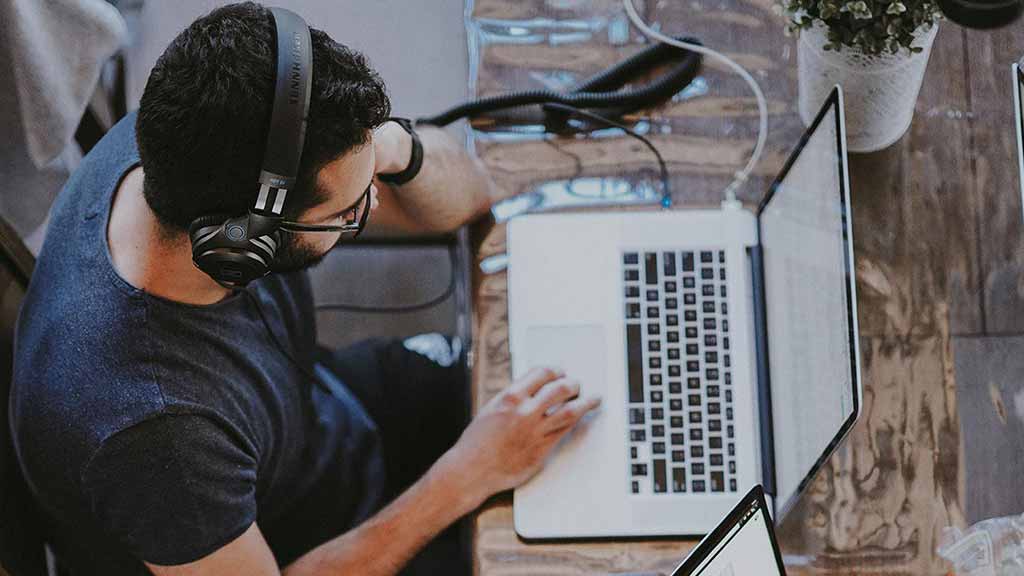 Mann mit Kopfhörern vor dem Laptop bei der digitalen Weiterbildung